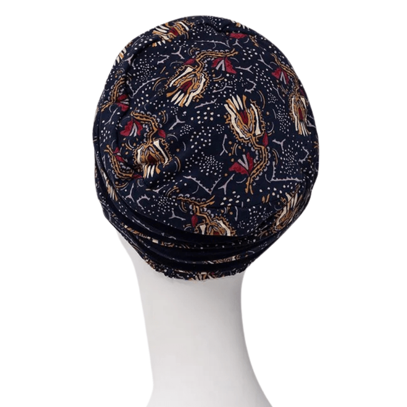 Shanti turban in Amber Garden print seen from the back on a white mannequin, with the dark blue feather and stem motif