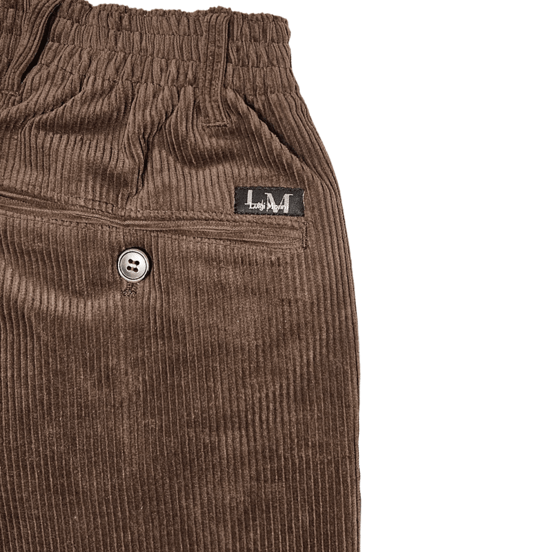 Tæt på detalje af brun fløjl, elastikkant, bæltestrop og baglomme med knap og brand-tag
