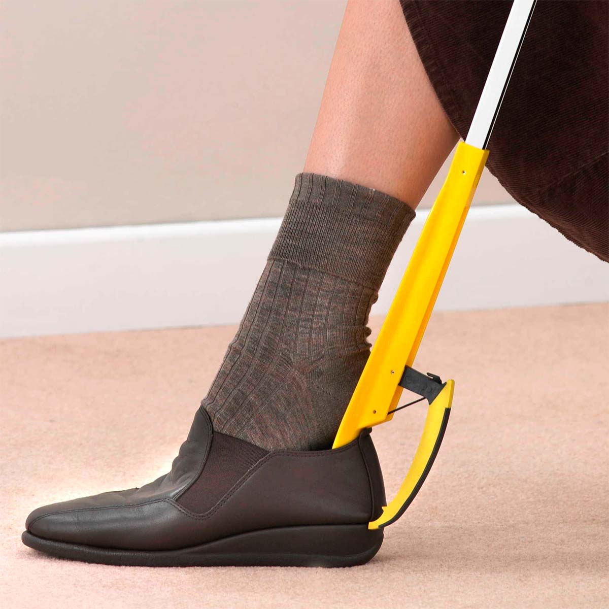 A person uses the yellow grabber as a shoehorn to put on a dark brown shoe