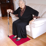Elderly woman sitting on a sofa with a walking stick and feet on a red non-slip mat