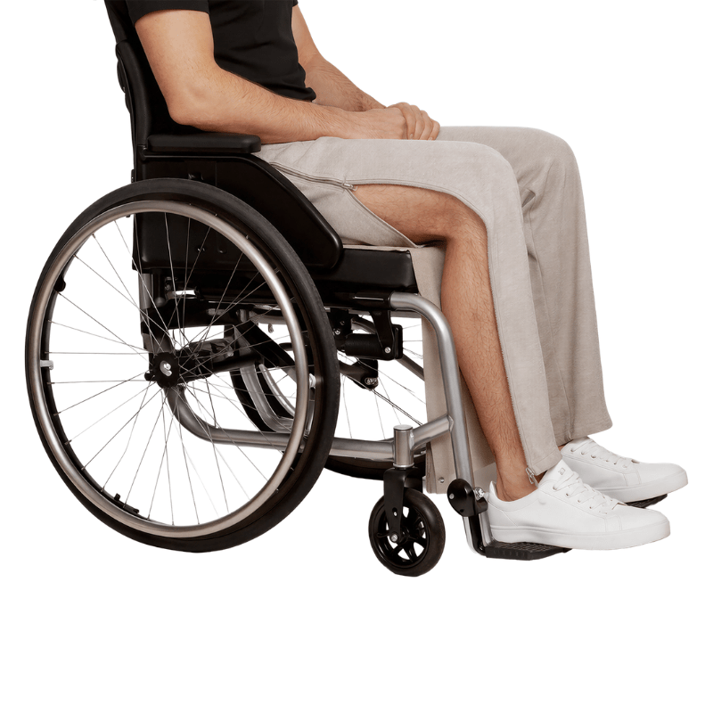 A person in a wheelchair wearing grey jogging pants with an open side zipper revealing the leg