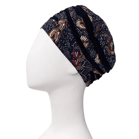 Shanti turban in Amber Garden print seen from the side on a white mannequin, with dark blue base and feather and stem motif