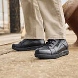 A man wearing beige trousers and black New Feet men's boots standing on a grey surface
